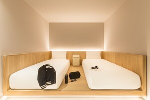 A compact room with two single beds, a small table, a backpack, and a suitcase.