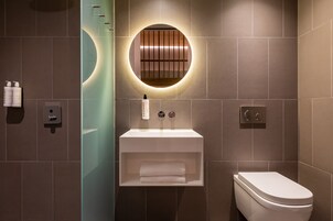 A modern bathroom with a white sink, a toilet, and a wall-mounted circular mirror.