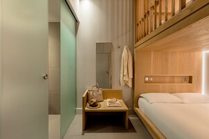 Ein kleines Hotelzimmer mit einem hölzernen Etagenbett, einem kleinen Schminktisch mit Spiegel und einem Nachttisch mit Handtuch und Hut.