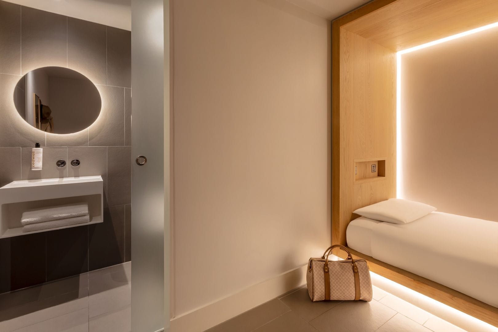 A modern bathroom with a vanity, a round mirror, and a wooden panel.