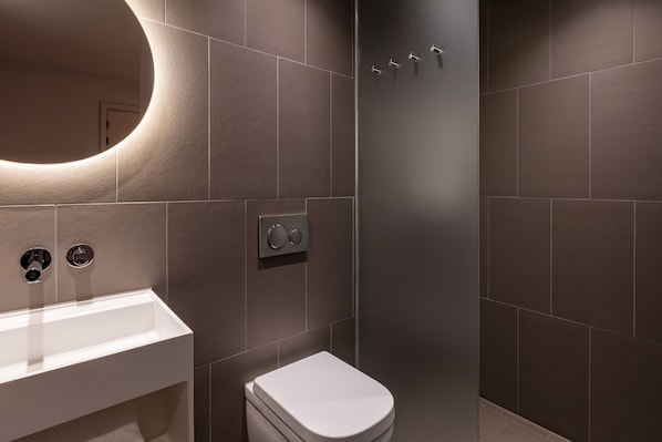 Un baño moderno con un lavamanos blanco, un inodoro y un panel de control de ducha instalado en la pared.