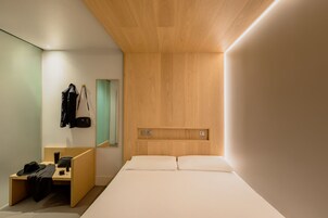 Ein modernes Hotelzimmer mit einem Holzkopfteil, einem Schreibtisch mit Stuhl, einem Spiegel und einem Bett mit weißen Bettbezügen.