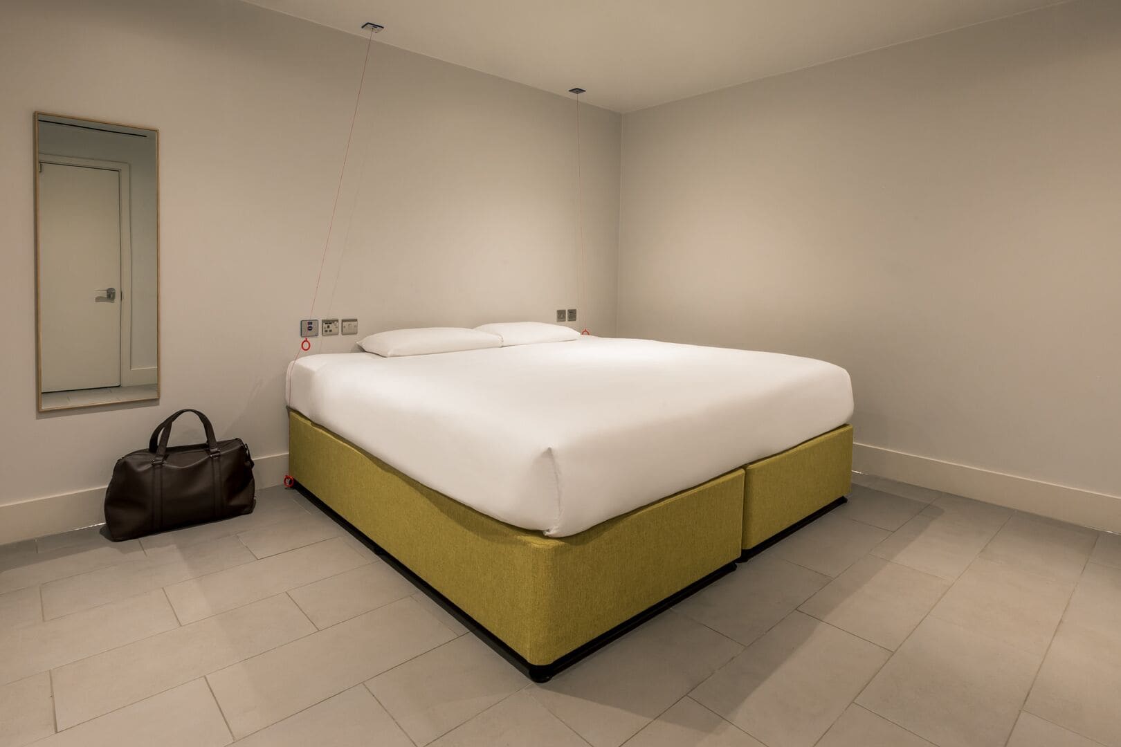 A modern bedroom with a bed, a mirror, a wall socket, and a bag.