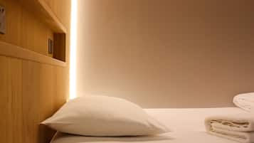 A neatly made bed with a white pillow and folded towels, wooden headboard, and a shelf with a small item on it.