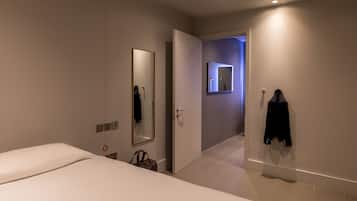 A modern hotel room with a large bed, a mirror, a coat rack, and a bathroom visible through an open door.