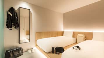 Une chambre d’hôtel moderne avec deux lits, un miroir, une tête de lit en bois, une table de chevet, un sac noir, une paire de chaussures et un sac à dos.