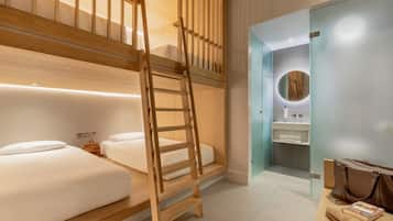 Habitación de hotel con literas, una escalera de madera, un baño con espejo y una mesita con un libro y una bolsa.