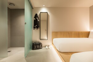 Ein modernes Hotelzimmer mit Dusche, Spiegel, Bett und Holz-Kopfteil.