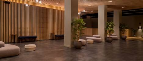 A modern lobby with a wooden slatted ceiling, large columns, and a variety of seating options including sofas and benches.