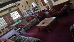 Uma sala de estar ampla com mesa de bilhar, assentos confortáveis e uma biblioteca.