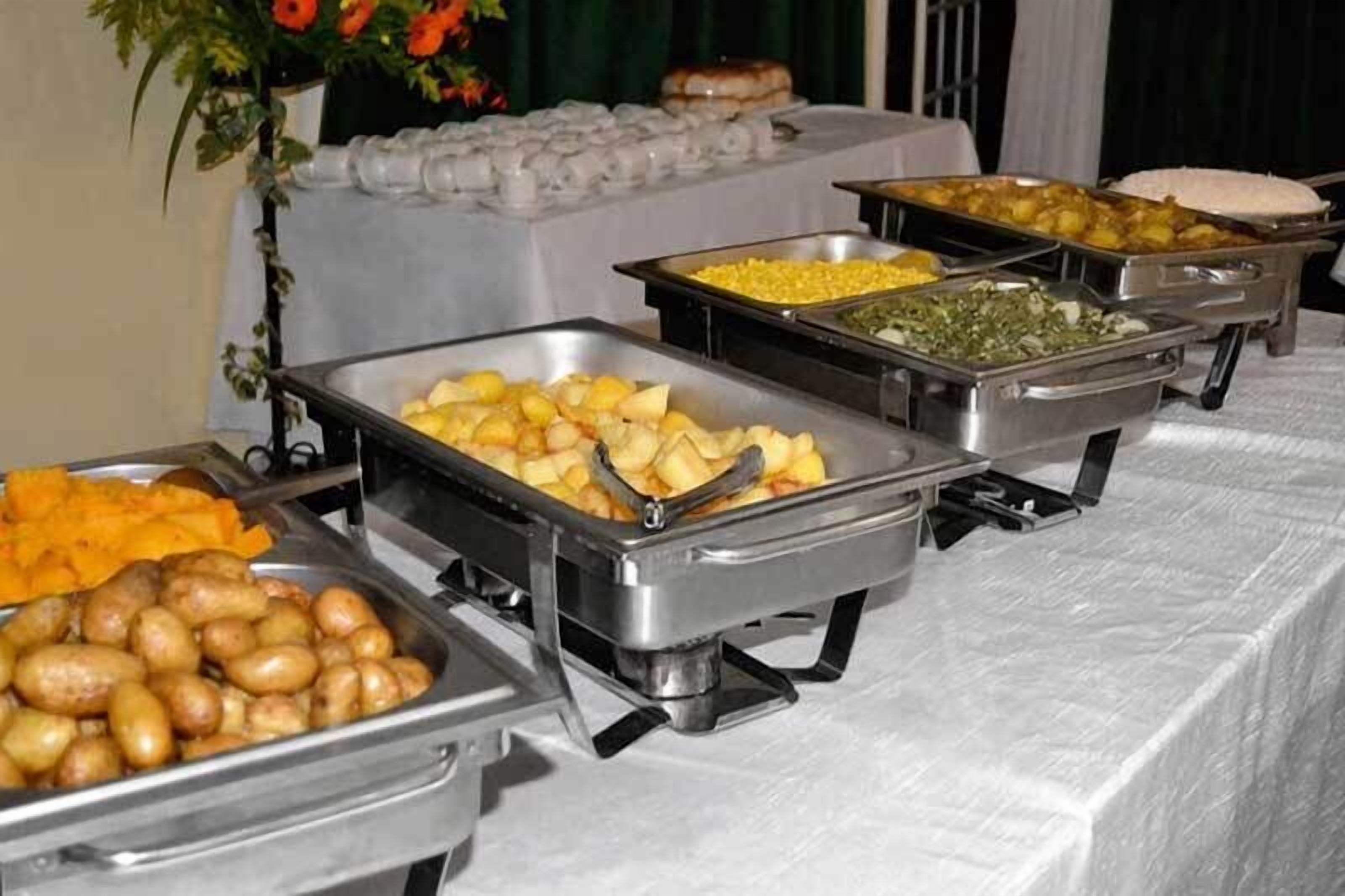 A buffet table with various food items including potatoes, corn, and other vegetables.