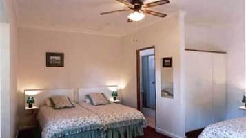 A bedroom with two beds, a ceiling fan, and a door leading to another room.