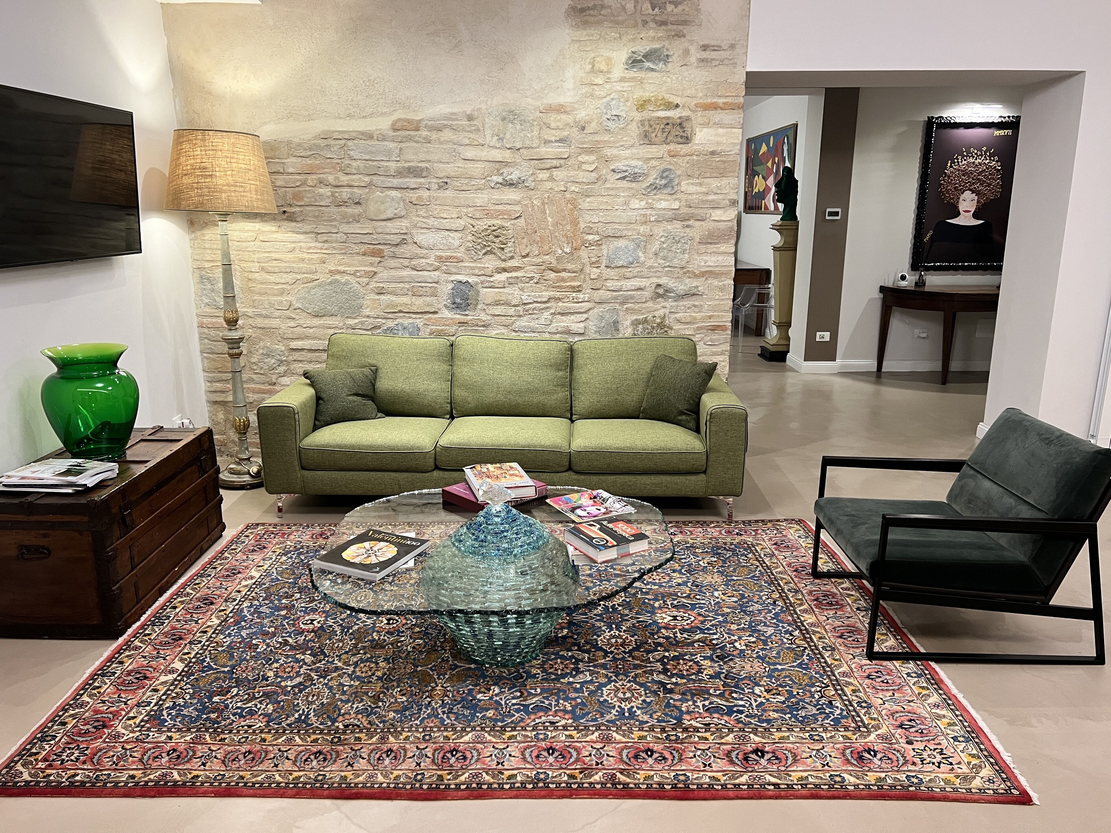 Una sala de estar con un sofá verde, una mesa de centro de vidrio, un tapete estampado y un jarrón verde.