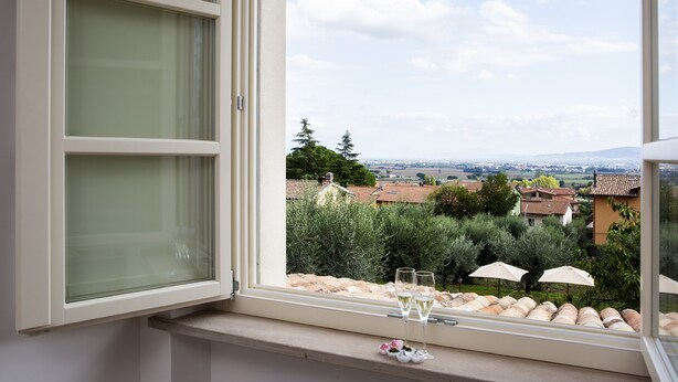 Ein Fenster mit Blick auf einen Weinberg und Häuser, zwei Gläser Weißwein und ein kleines dekoratives Objekt auf der Fensterbank.