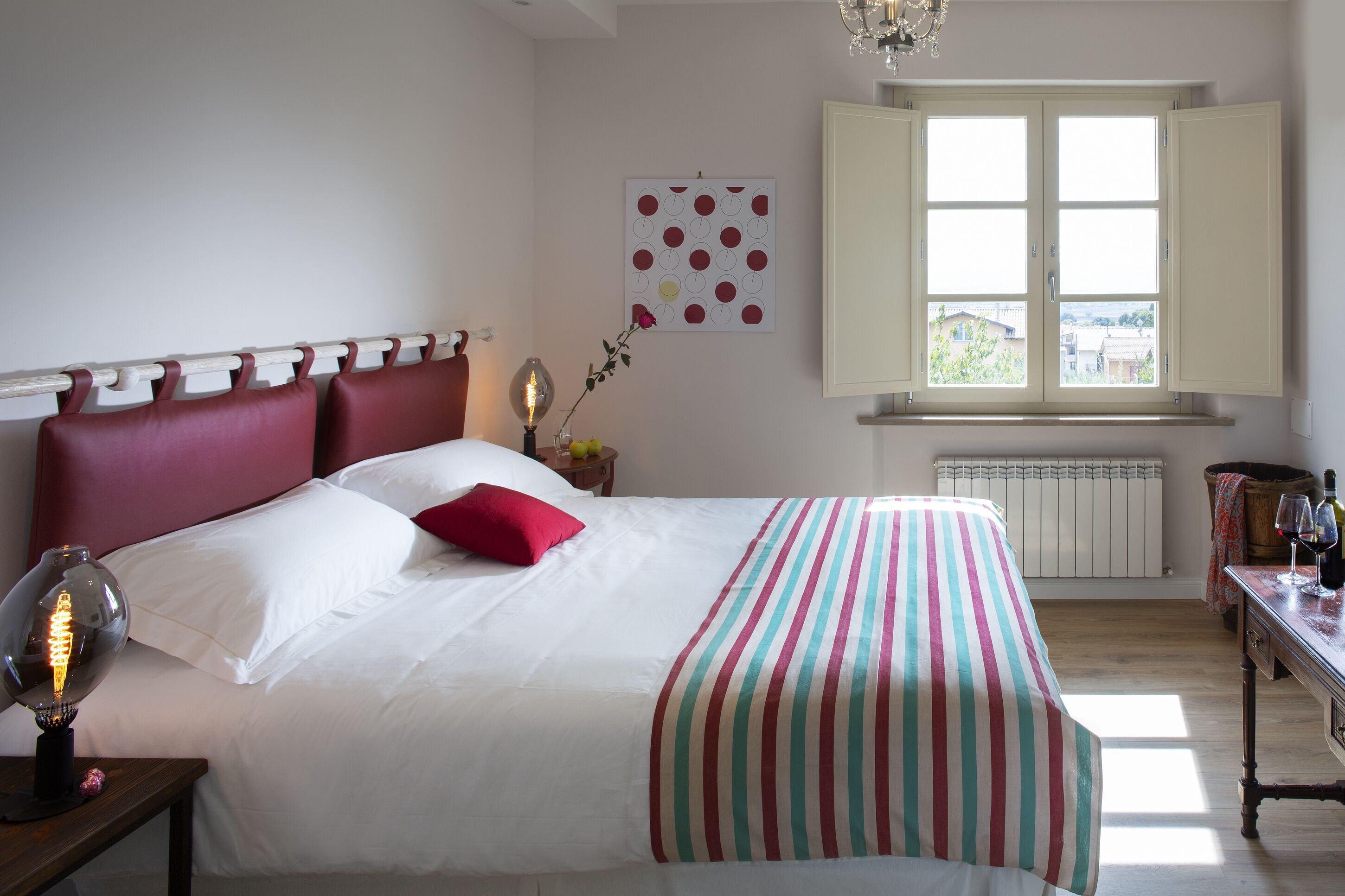 Un lit bien fait, avec une couvre-lit à rayures, un oreiller rouge et une lampe de chevet.