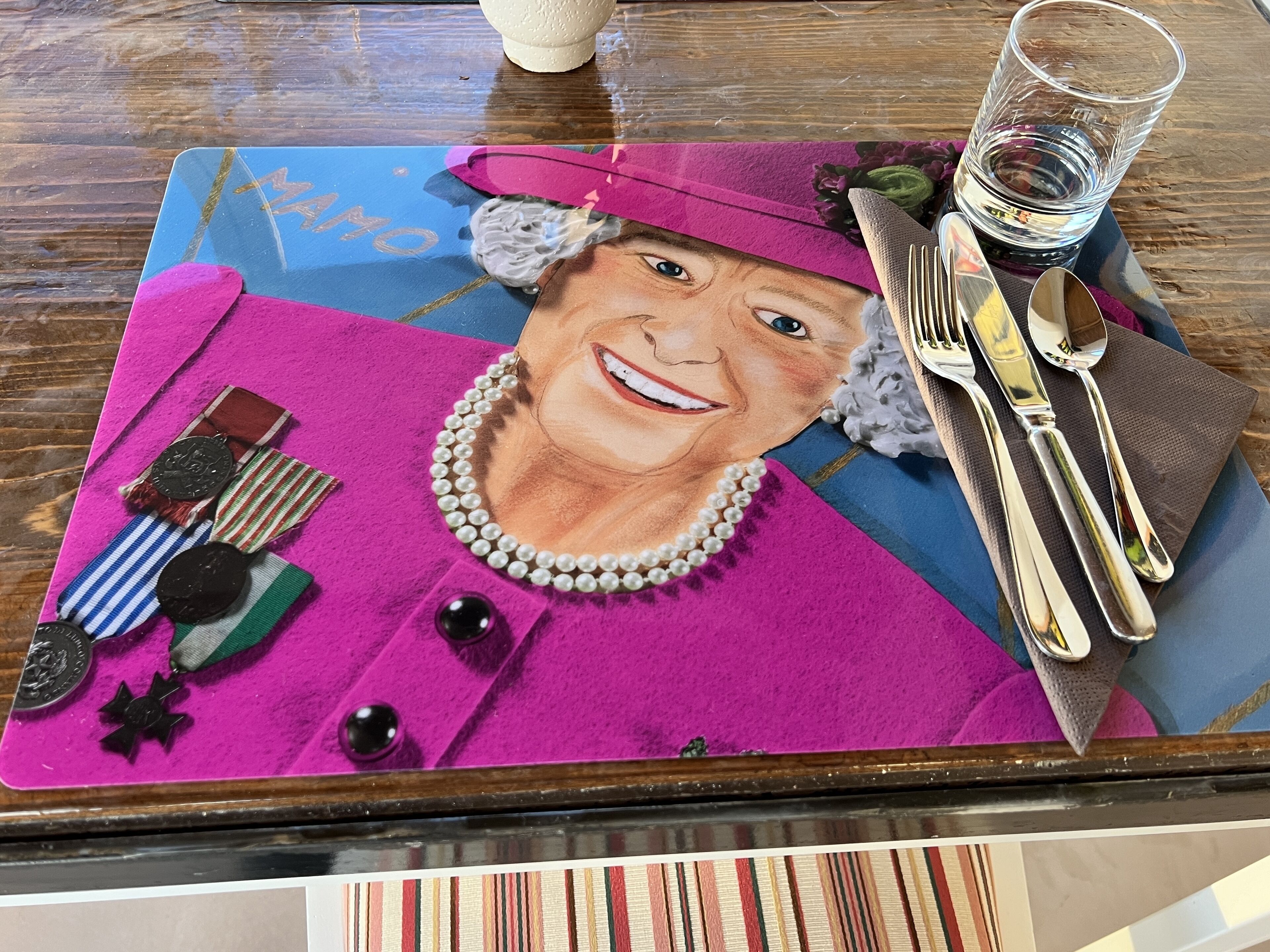 A table with a colorful mat, a glass of water, and a set of cutlery.