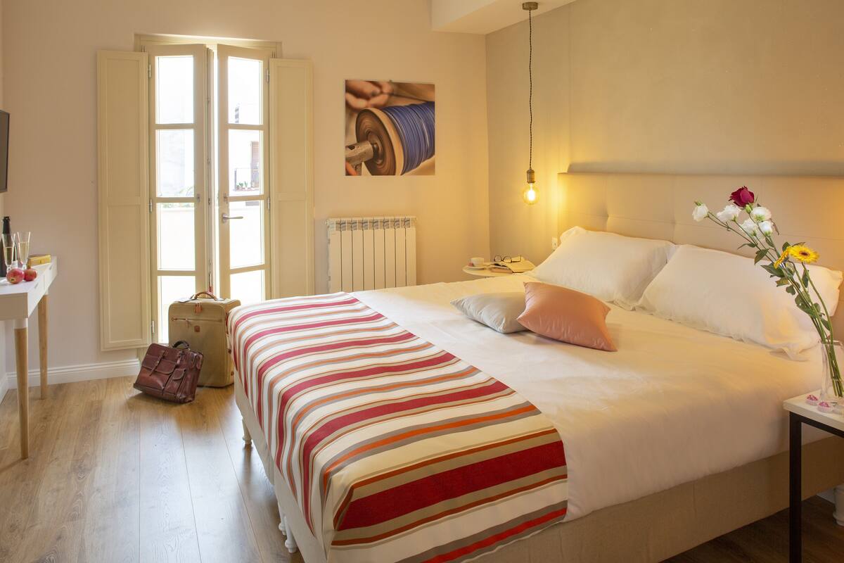 A hotel room with a bed, bedside table, lamp, and a window with curtains.