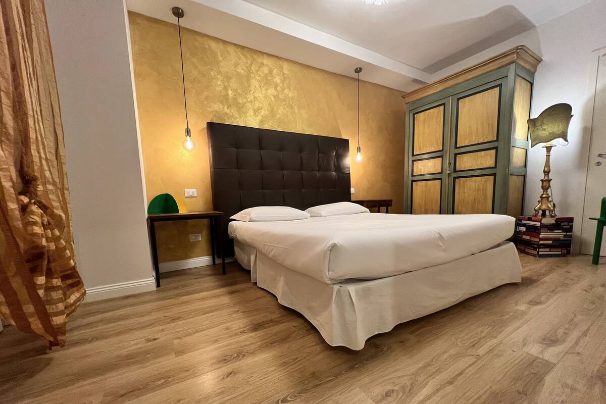 A bedroom with a large bed, a nightstand, a dresser, and a lamp.