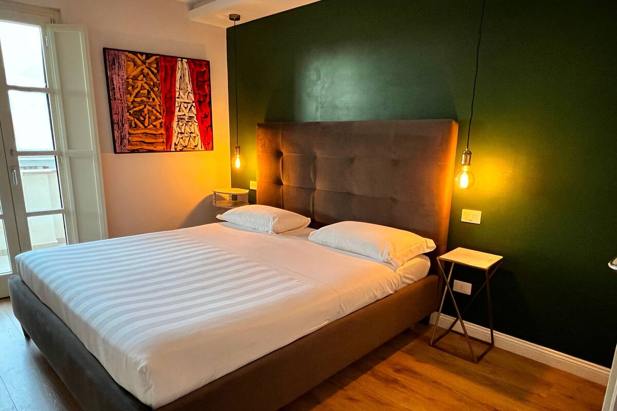 A bedroom with a large bed, a headboard, two bedside tables, and a wall-mounted light fixture.