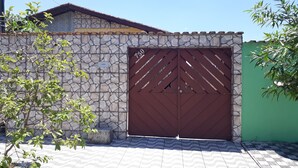 A stone wall with a metal gate, a tiled entrance, and a green fence. - SEASON IN MONGAGUÁ (Balneario Itaguaí)