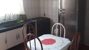 A kitchen with white tiled walls, a stainless steel refrigerator, a stove, and a dining table with chairs. - SEASON IN MONGAGUÁ (Balneario Itaguaí)