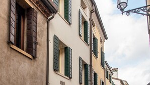 A cobblestone street with historic buildings featuring arched doorways and green shutters. - Casa Giotto (Padova)