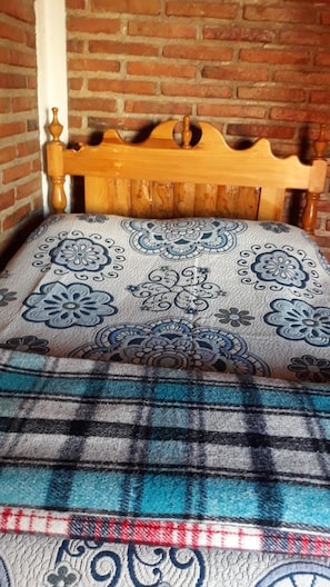 Una cama con cabecera de madera, almohada estampada y manta escocesa.