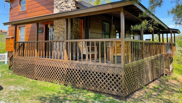 A two-story wooden cabin with a stone chimney, a covered porch, and a wooden fence. - Pet friendly/Hot tub/High speed internet/Location! (Sevierville)