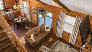 A cozy cabin interior with a wooden dining area, a sofa with decorative pillows, a ceiling fan, and a television. - Pet friendly/Hot tub/High speed internet/Location! (Sevierville)