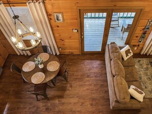 A cozy cabin interior with a wooden dining table, a sofa, and a chandelier.