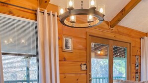 A wooden interior with a dining table set for four, surrounded by chairs. A chandelier hangs above the table, and there is a window with blinds to the left. - Pet friendly/Hot tub/High speed internet/Location! (Sevierville)