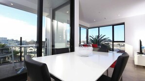 A modern dining area with a white table, black chairs, and a large window offering a city view.