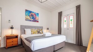Et hotelværelse med en stor seng, et natbord, en lampe, et billede på væggen og en dør med gardiner.