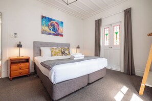 A hotel room with a large bed, a bedside table, a lamp, a painting on the wall, and a door with curtains.