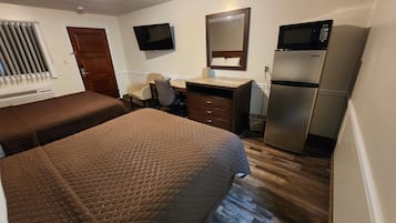 A hotel room with two beds, a desk, a chair, a TV, a microwave, and a refrigerator.