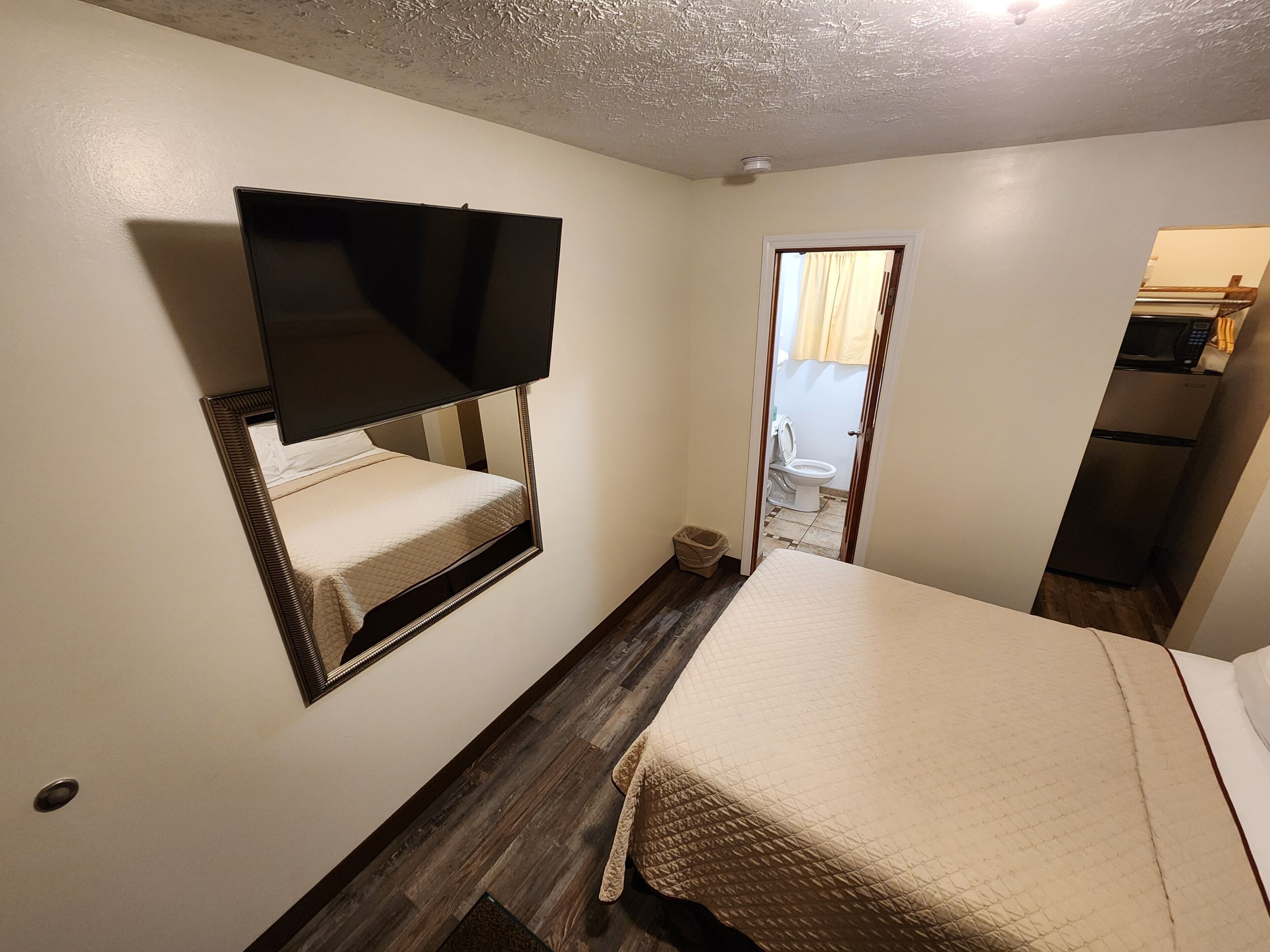 Una habitación pequeña y acogedora con una cama, un televisor montado en la pared y una puerta que da a un baño.