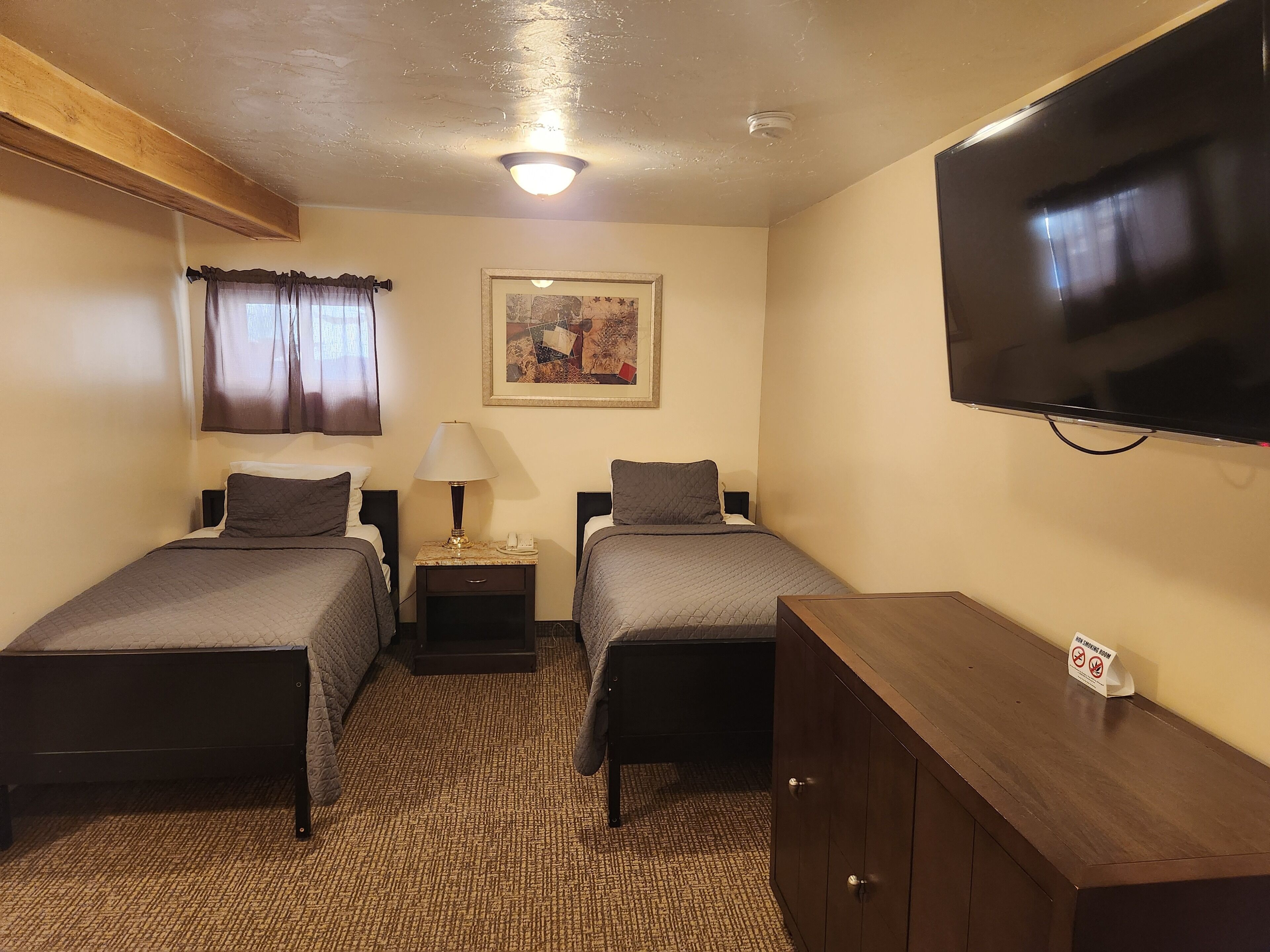 A hotel room with two beds, a television, a painting, and a wooden cabinet.