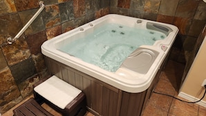 A hot tub with a wooden bench and a step, set against a stone wall.