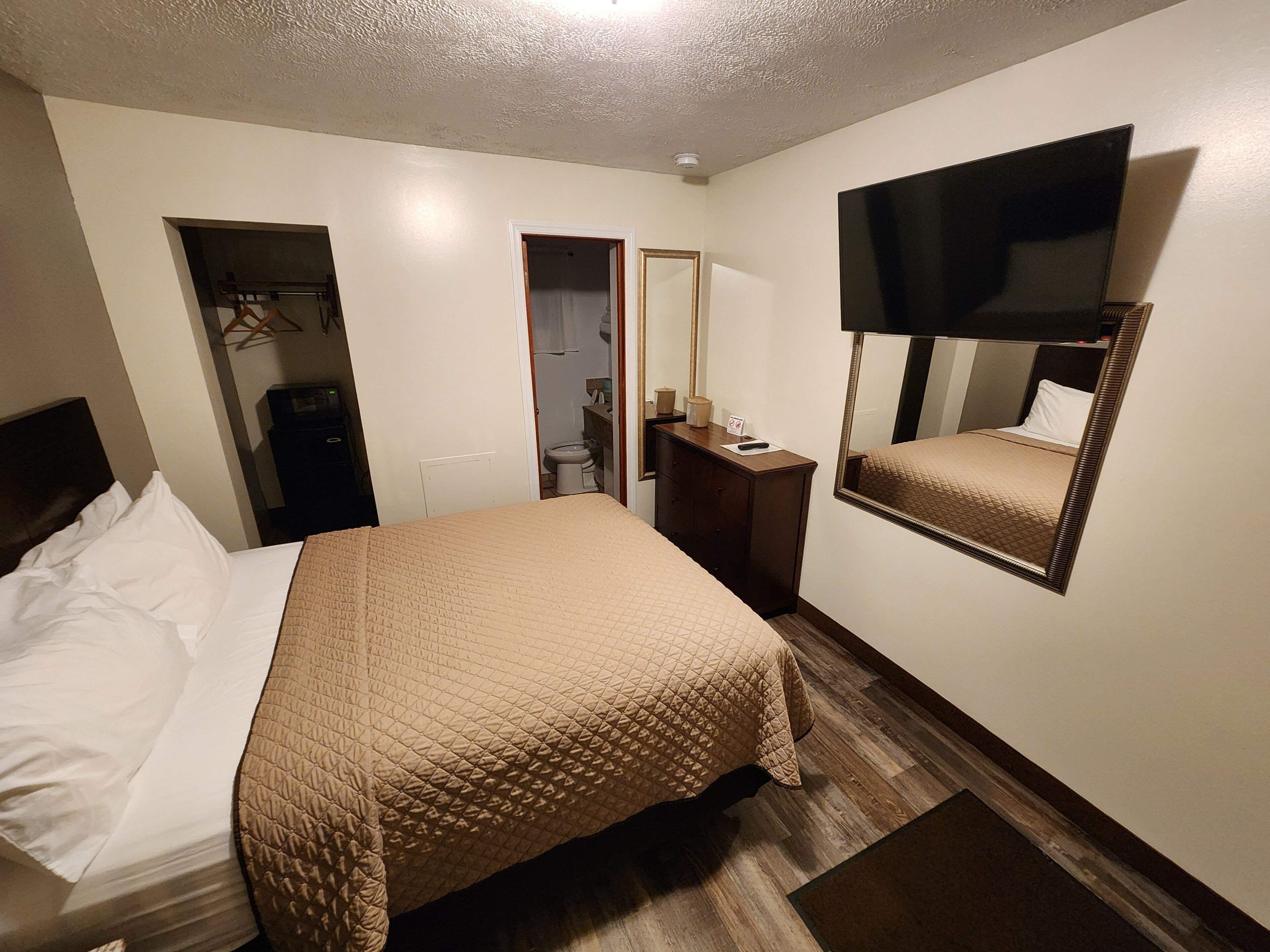 Quarto de hotel com cama, cômoda, espelho e televisão.