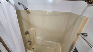 A corner bathroom with a bathtub, a shower, and a handrail.
