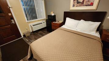 Habitación de hotel con cama, mesita de noche, teléfono, radiador y ventana con persianas.