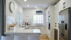 Een moderne keuken met een marmeren eiland, witte barkrukken, roestvrijstalen apparatuur en een groot raam met zonwering.