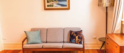 A living room with a sofa, a framed landscape painting, a lamp, and a wooden dresser.