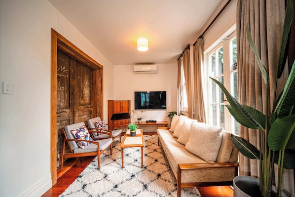 A living room with a sofa, chairs, a coffee table, a TV, and a large window with curtains.