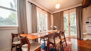 A dining room with a wooden table, four chairs, a patterned rug, and large windows with curtains. - Freemans Bay 3BDR Stylist Villa (Auckland)