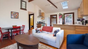 A spacious living area with a dining table, red chairs, a white sofa, and a blue armchair. A kitchen is visible in the background with wooden cabinets and a window. - Curtis Cottage · Berkeley Cottage, comfy, stylish, good wifi (Berkeley)