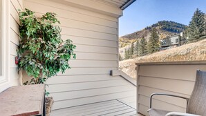 A covered patio with a table and chair, a potted plant, and a view of a mountain and trees. - Family Condo w Mtn Views, walk to Gondola, SV22D (Vail)