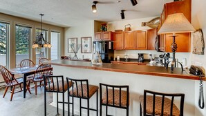 A spacious kitchen with wooden cabinets, a central island with seating, and pendant lighting. - Family Condo w Mtn Views, walk to Gondola, SV22D (Vail)