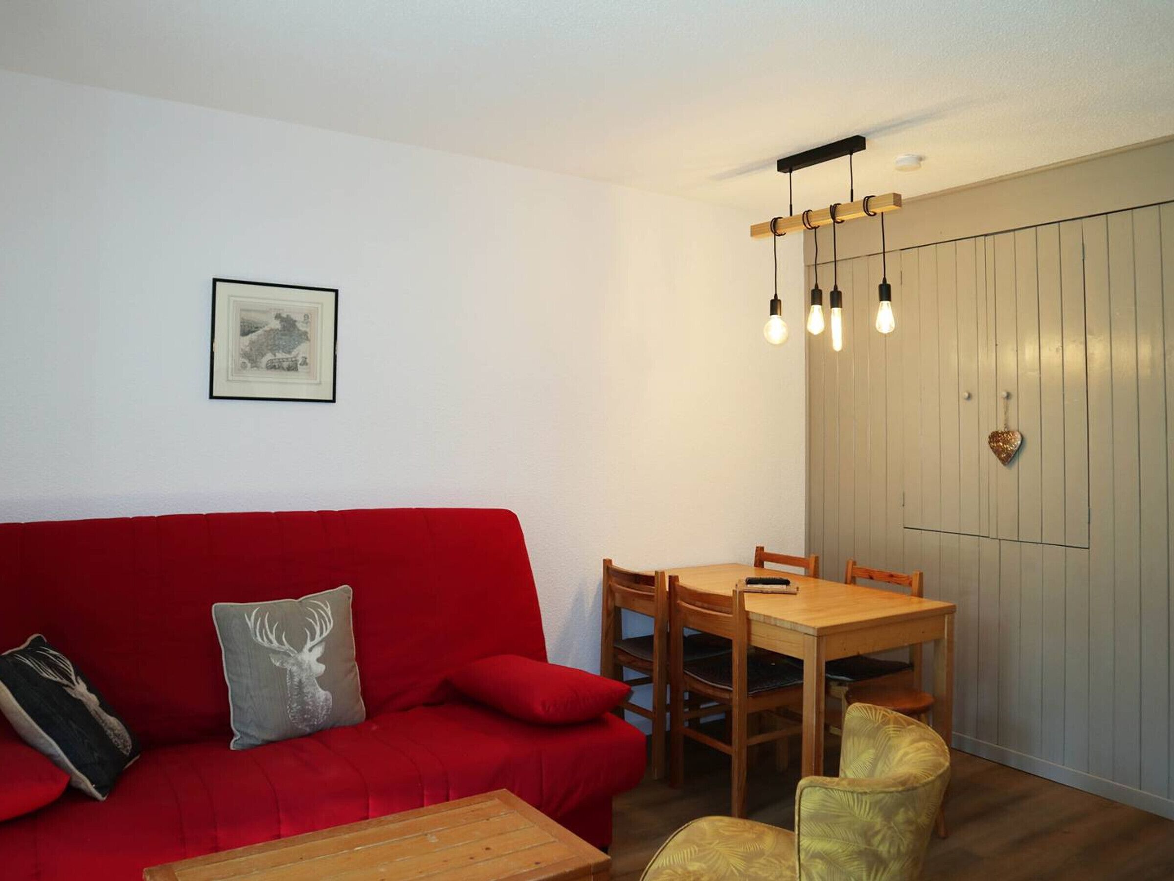 A red sofa with a deer pillow, a wooden dining table with chairs, and a hanging light fixture.