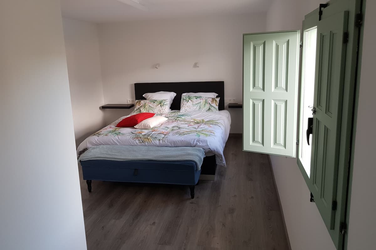 A bedroom with a bed, a nightstand, a blue bench, and a green door.
